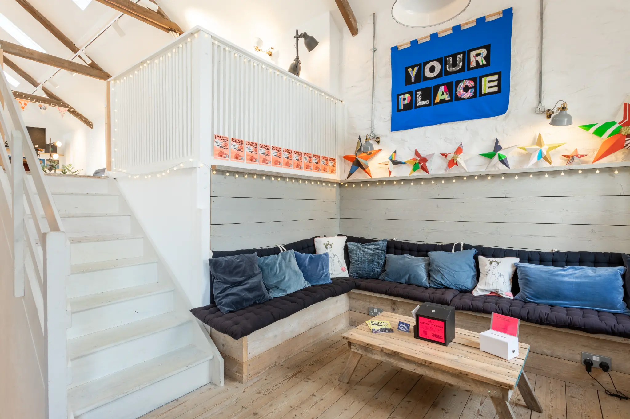 Cosy lounge area with built-in seating, blue cushions, fairy lights, and "Your Place" banner