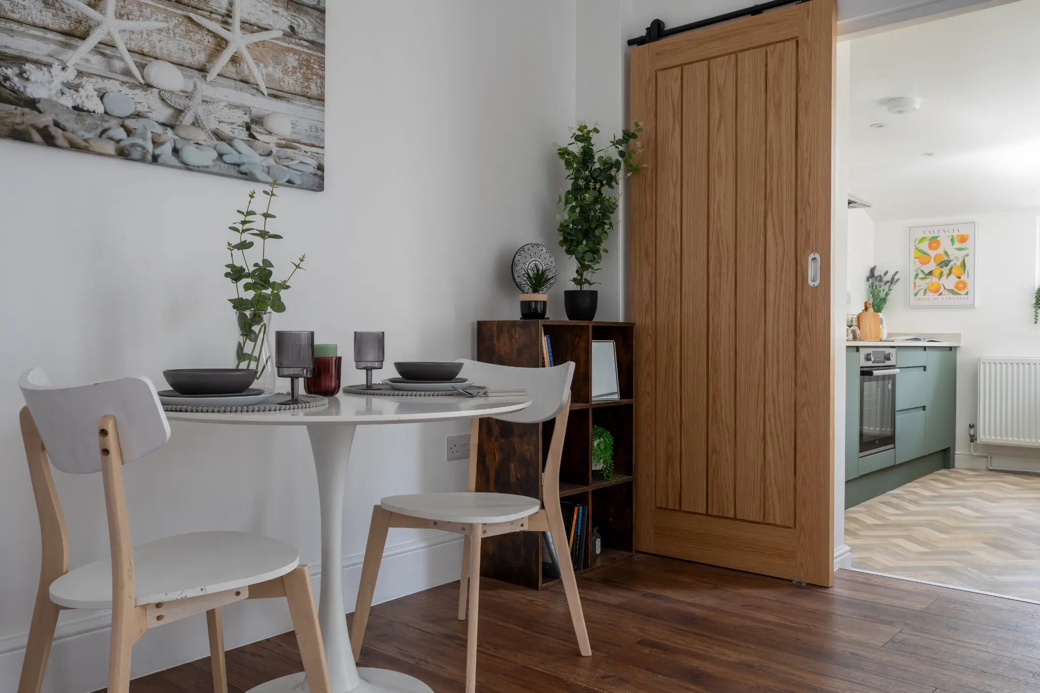 Dining area with round white table, beach art and oak barn door in renovated Bristol home
