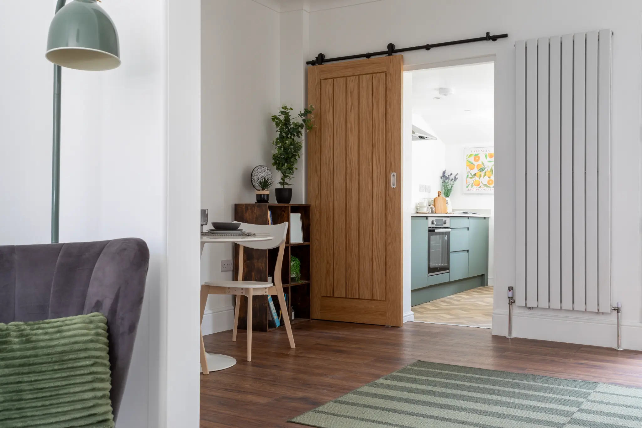 Oak sliding barn door connecting hallway to sage green kitchen with vertical radiator