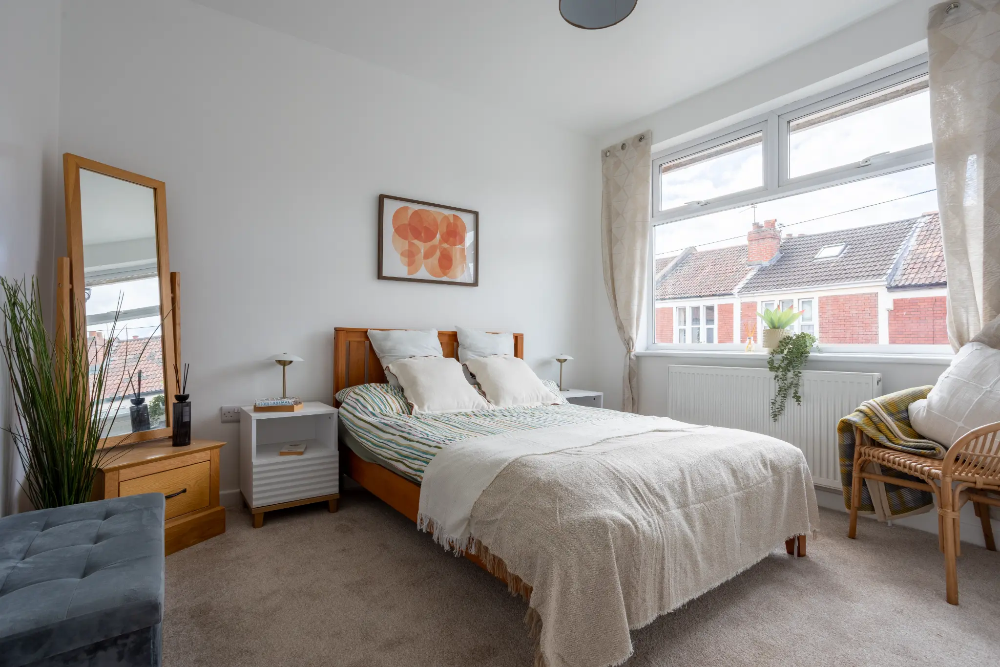 Master bedroom with wooden bed frame, standing mirror and rattan chair in Bristol renovation