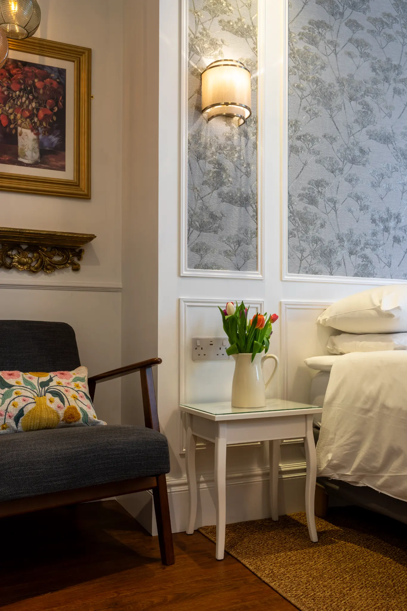 Bedside detail with chair, tulips, and wallpaper at Ferndale Mews