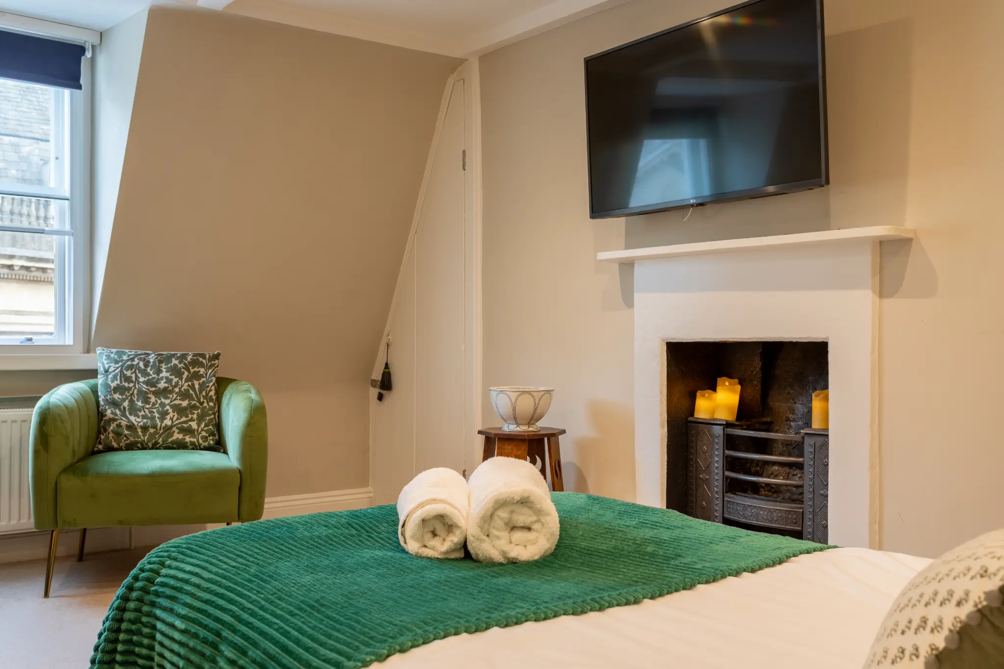 Cosy bedroom with green throw, fireplace, and wall-mounted TV at Milsom Apartments