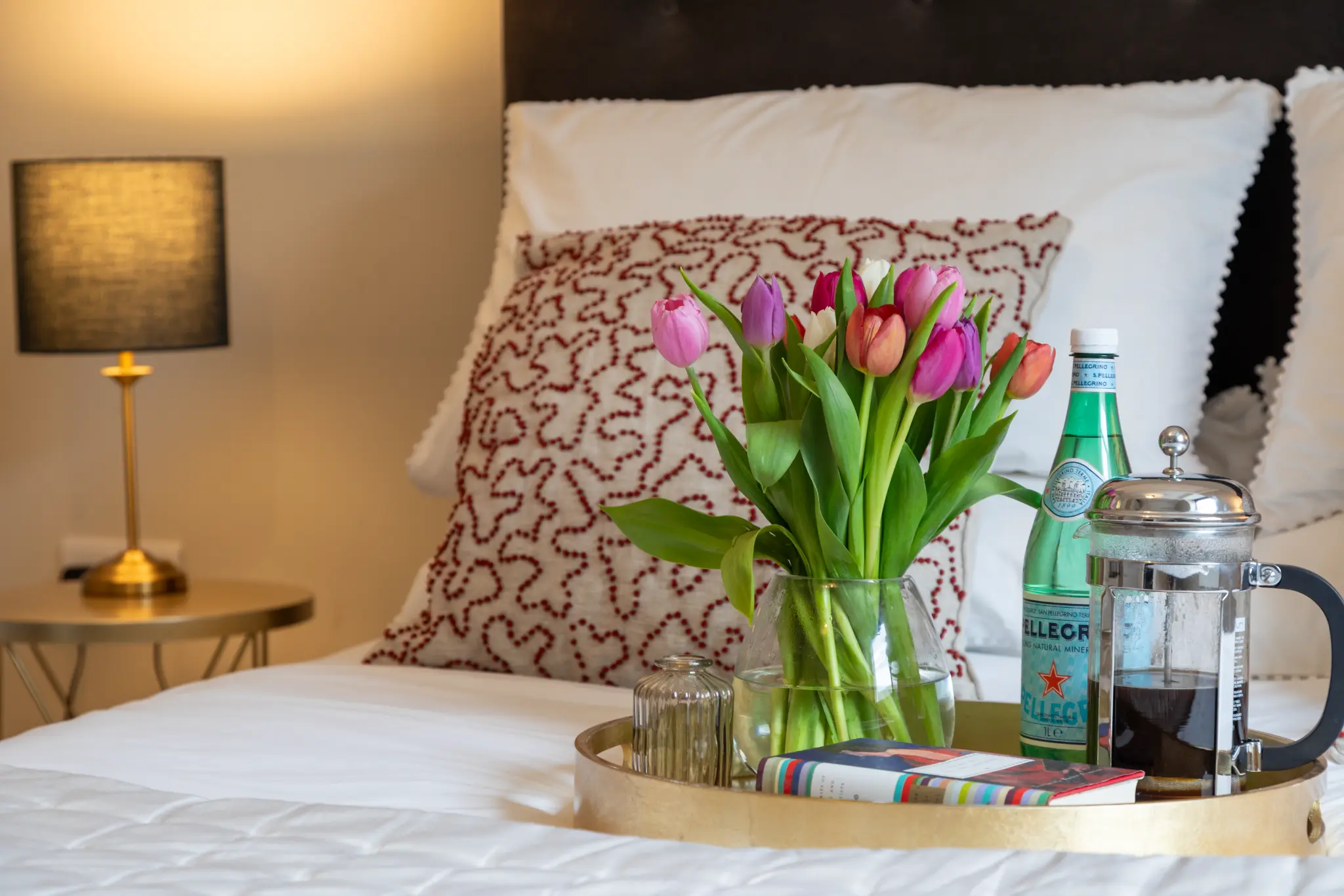 Close-up of welcome tray with tulips, coffee press, and sparkling water on bed