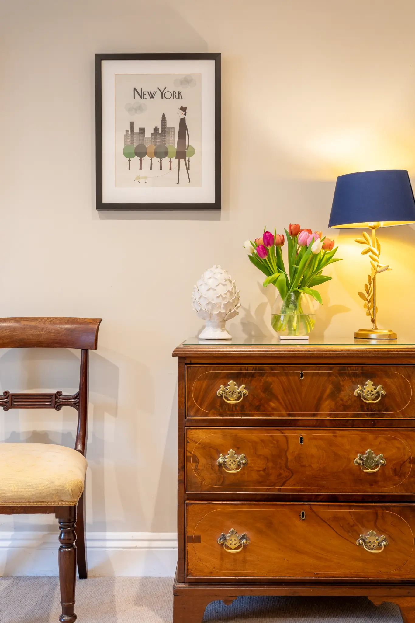 Antique mahogany chest with tulips, lamp, and New York print at Milsom Apartments