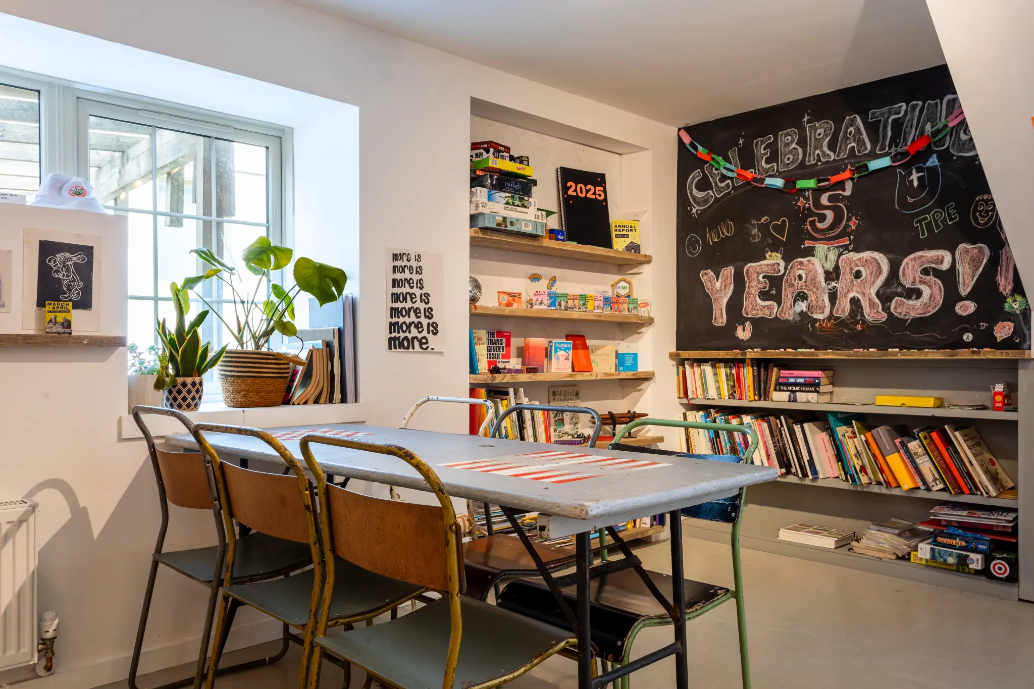 Library area with bookshelves, vintage furniture, plants, and "Celebrating 5 Years" chalkboard