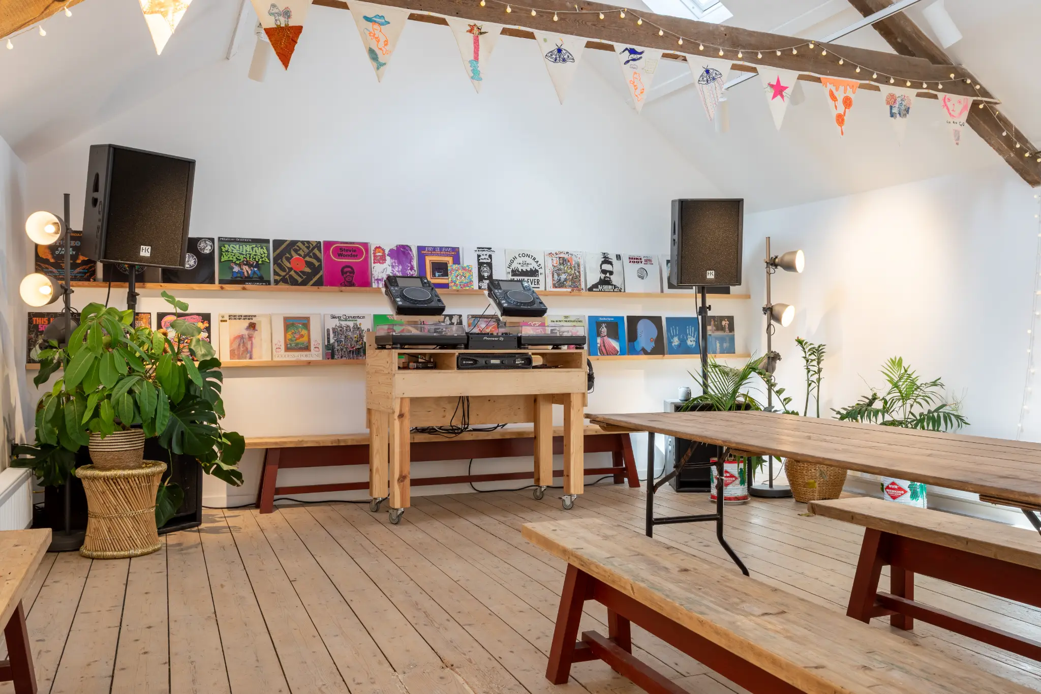 Close-up of the DJ booth with Pioneer turntables, vinyl records, speakers, and plants