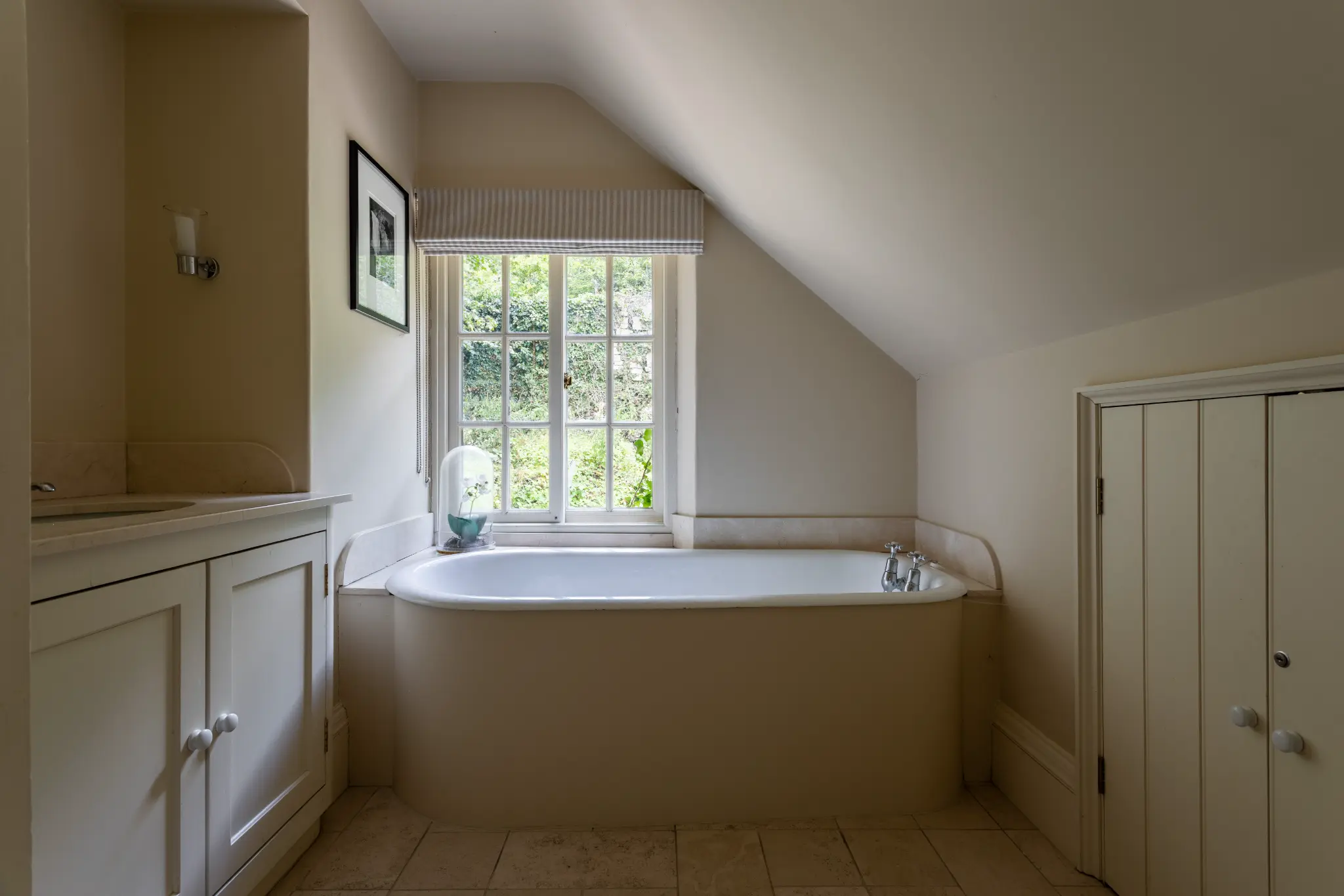 Charming en suite bathroom featuring a built-in bathtub beneath a multi-pane window, neutral tones, and classic cabinetry in a historic manor