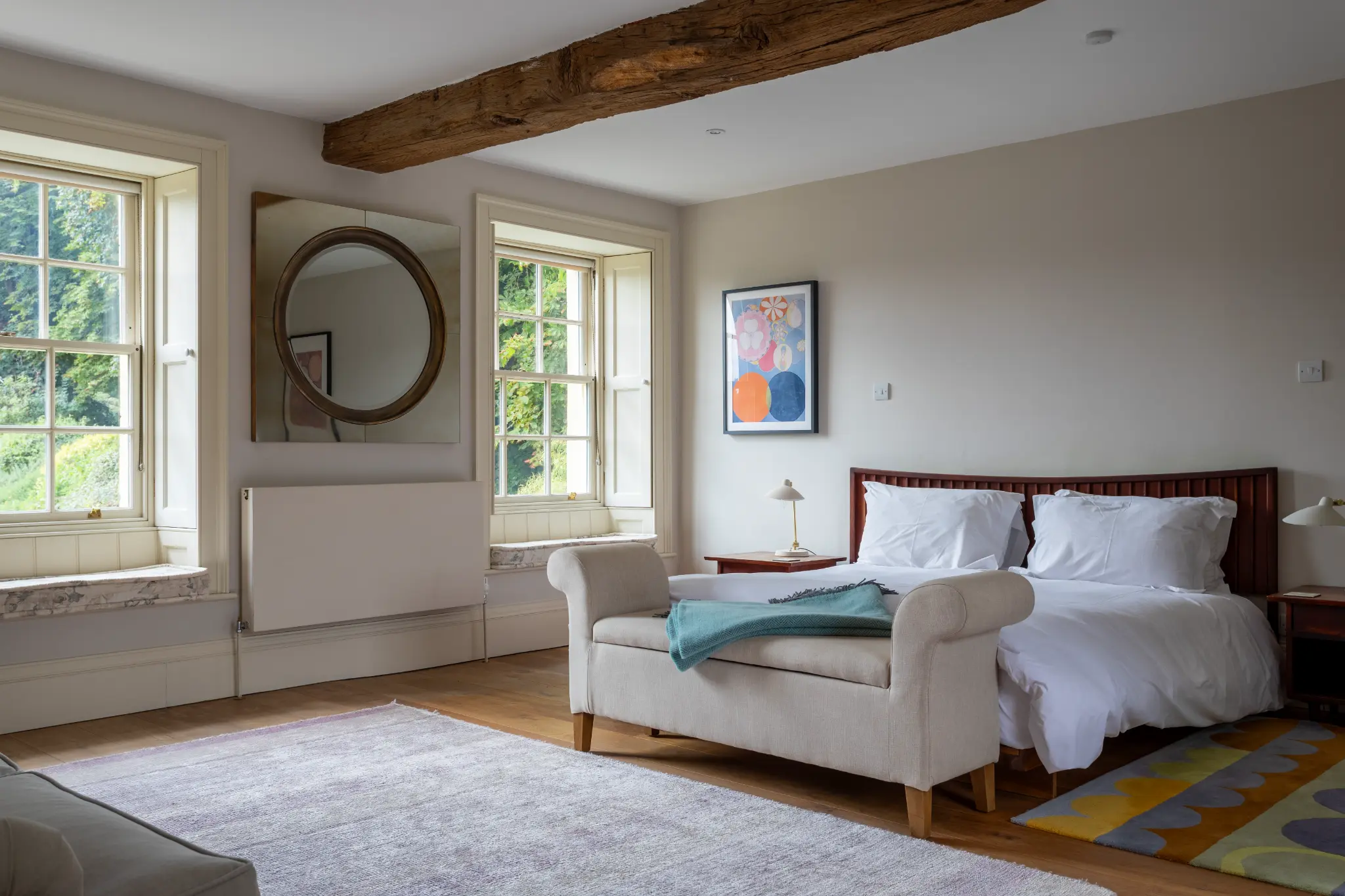 Bright and spacious luxury bedroom featuring rustic wooden ceiling beams, crisp white linens, and elegant contemporary furnishings at a Bath manor