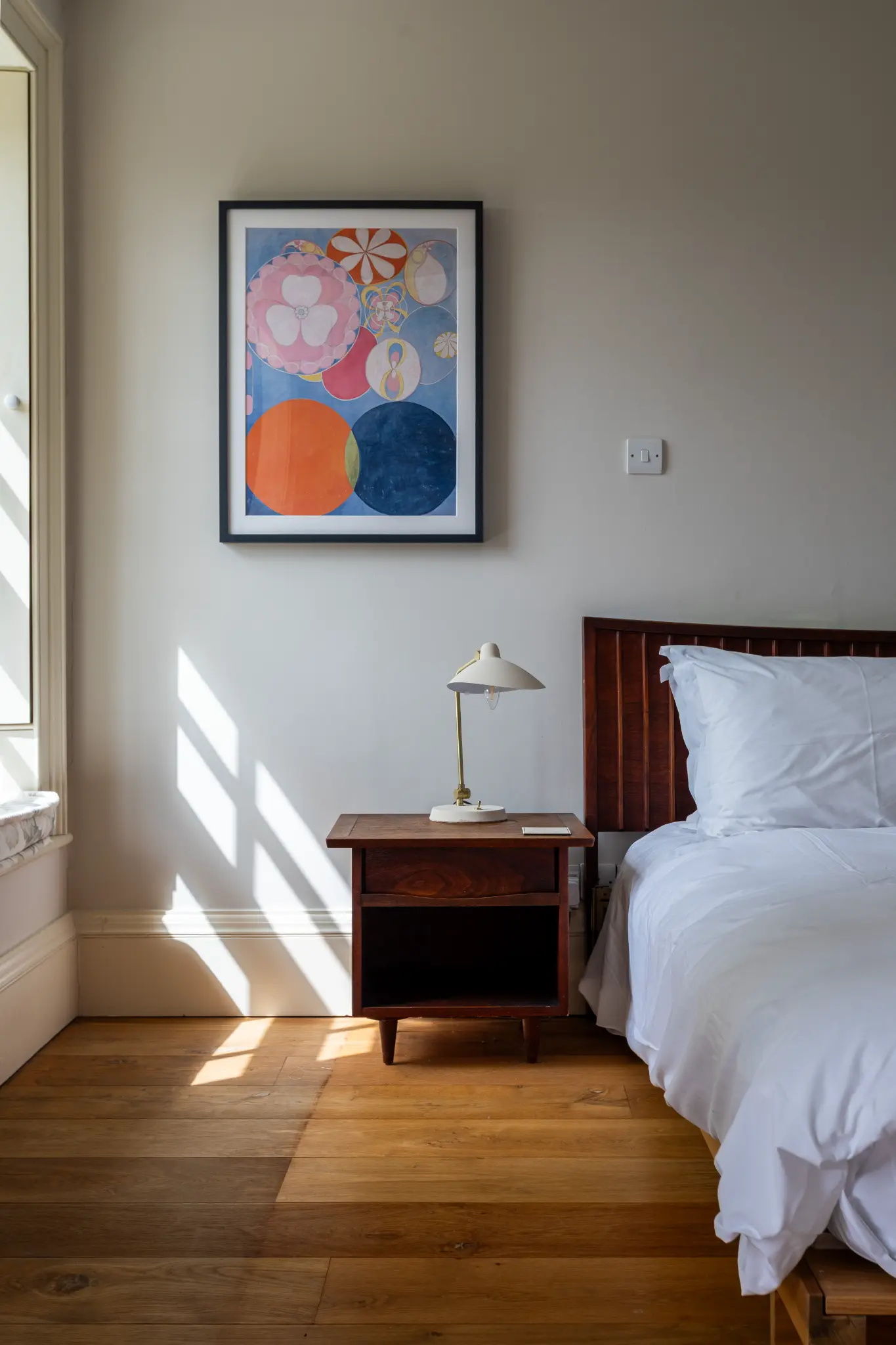 Bright bedroom corner in a luxury Bath manor featuring crisp white linens, a wooden nightstand, and vibrant abstract art