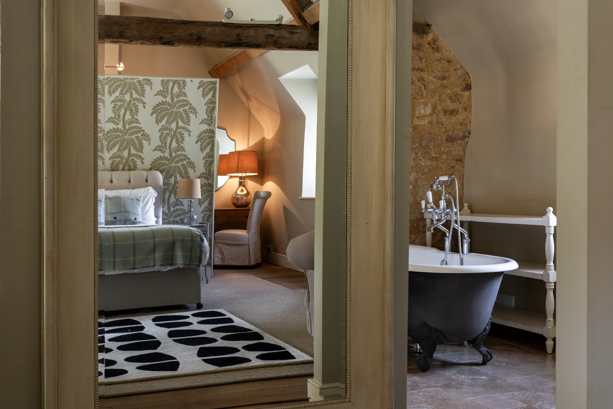 Luxurious bedroom suite with exposed wooden beams, a freestanding bathtub against rustic stone walls, and elegant furnishings at a Bath manor