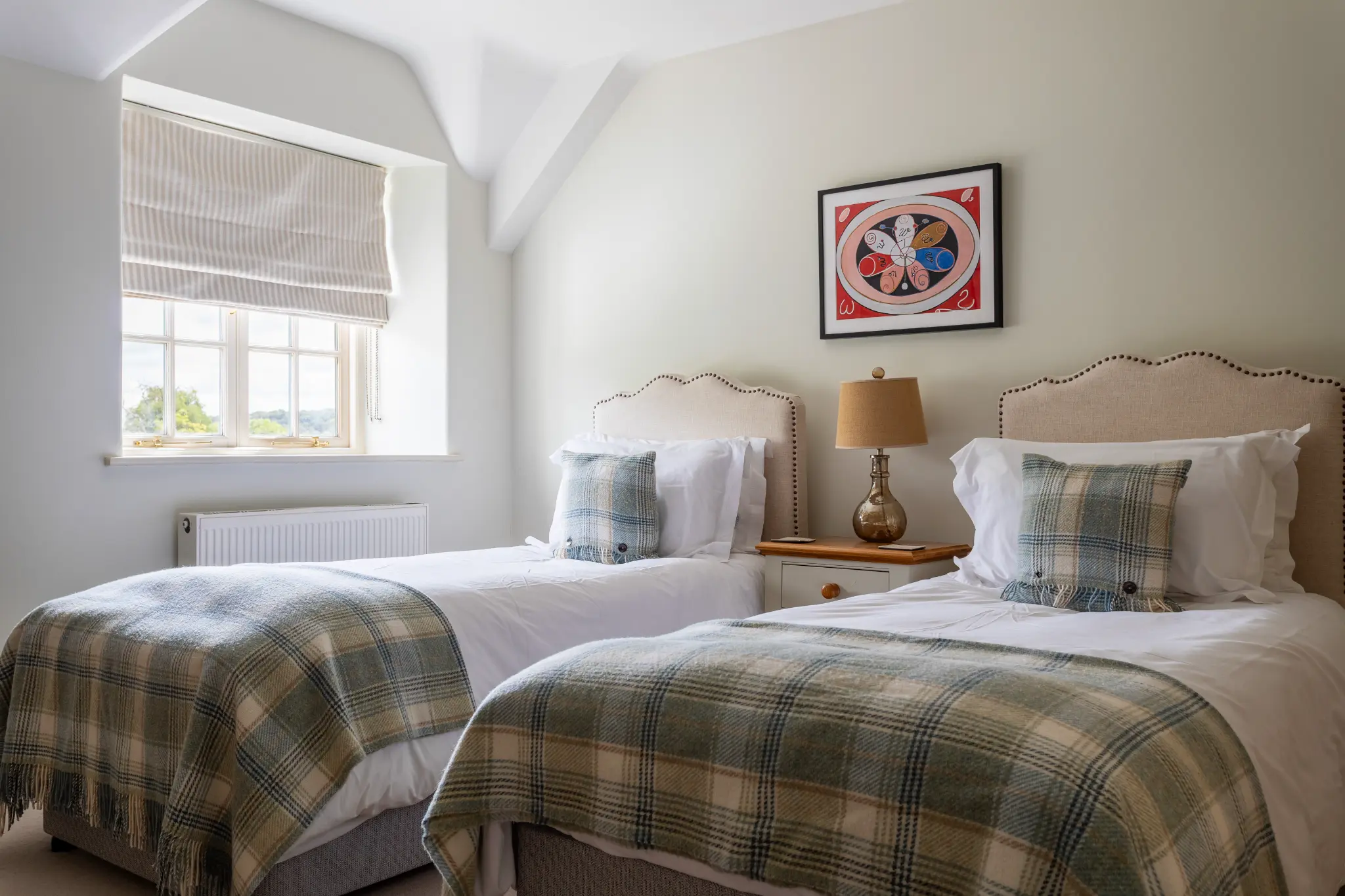 Cozy twin bedroom at a luxury Bath manor featuring plush plaid throws, elegant upholstered headboards, and historic architectural features