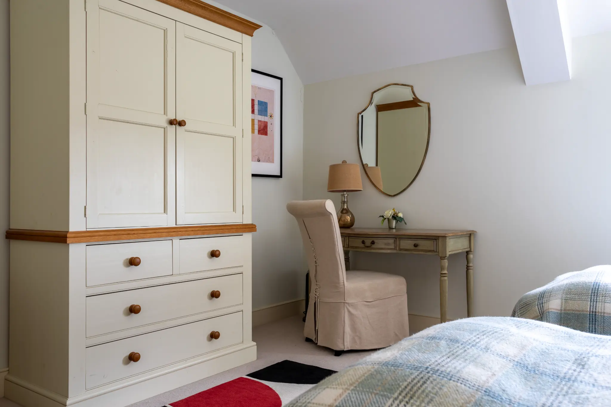 Charming twin bedroom corner featuring cream wooden wardrobe, dressing table, upholstered armchair, and slanted ceiling at a luxury Bath manor
