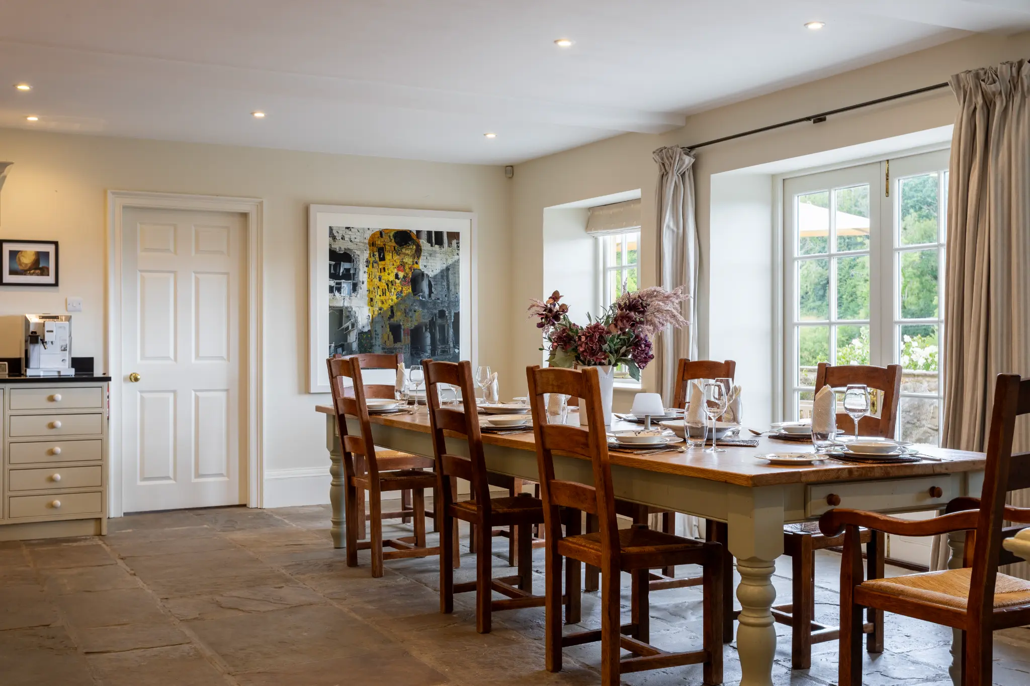 Sophisticated dining room at a luxury Bath manor featuring a large wooden farmhouse table, elegant place settings, and French doors