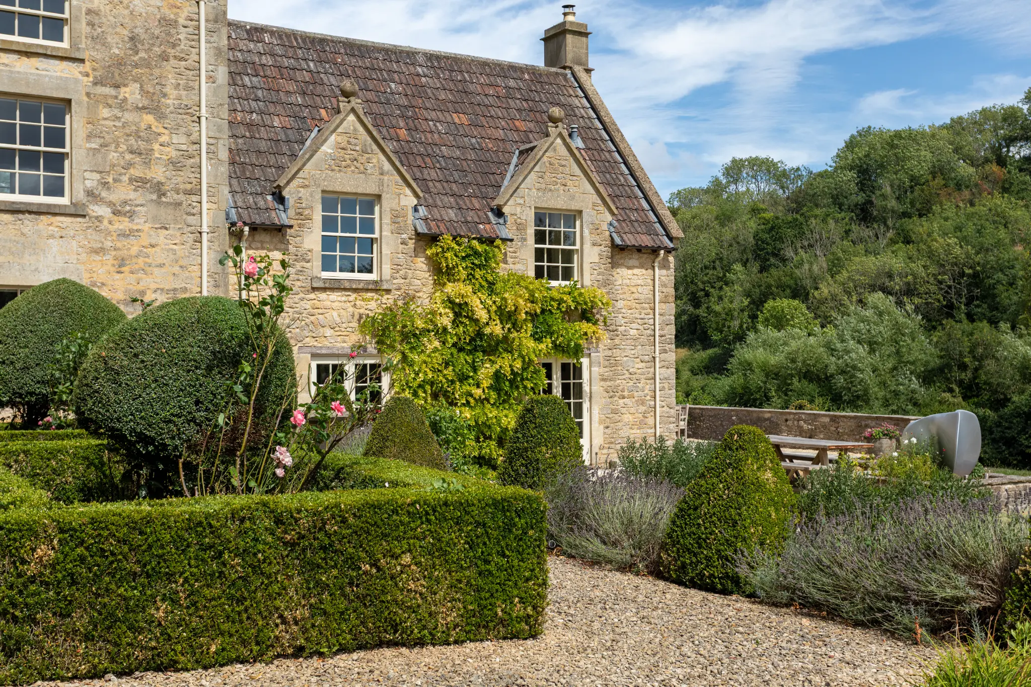 Manicured boxwood topiary and stone architecture at a luxury Bath manor with formal gravel path