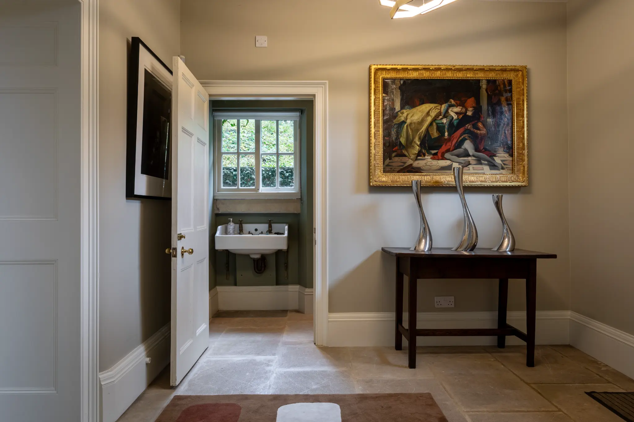 Elegant hallway with classic flagstone floors, dark wood console table, silver sculptures, and a traditional oil painting at a luxury Bath manor