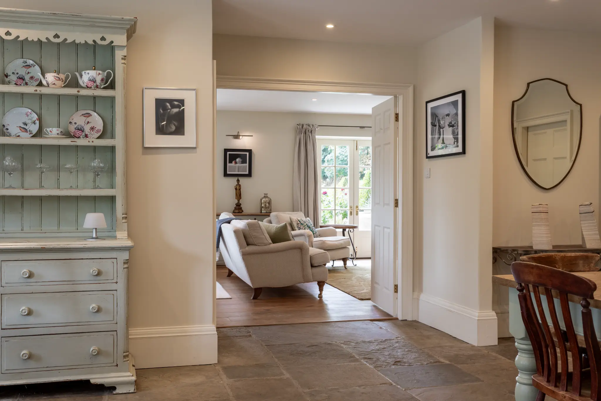 Elegant hallway view looking into a bright sitting room at a luxury Bath manor featuring rustic stone flooring and antique dresser