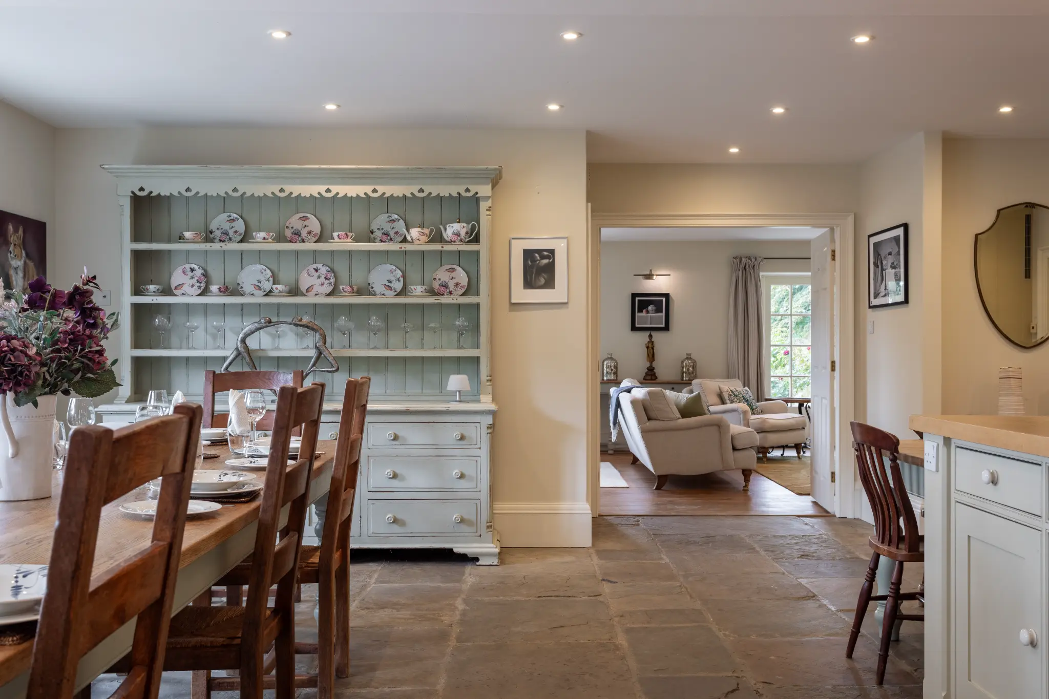 Spacious dining area with a large rustic wooden table, sage green dresser with fine china, and stone flagstone flooring at a luxury Bath manor