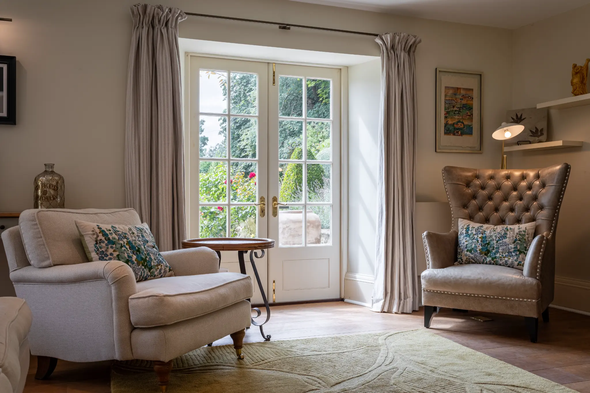Cozy living room with French doors opening to a lush garden, comfortable armchairs, and elegant styling at a luxury Bath manor