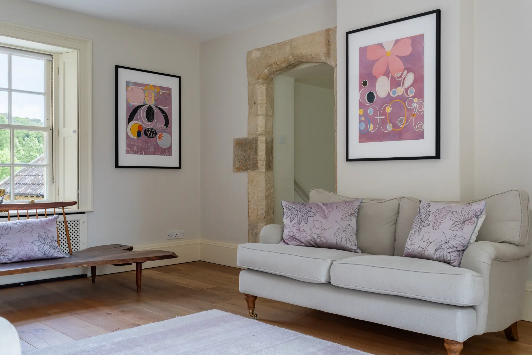 Bedroom with a light grey sofa, stone-arched doorway, and contemporary floral artwork at a luxury Bath manor