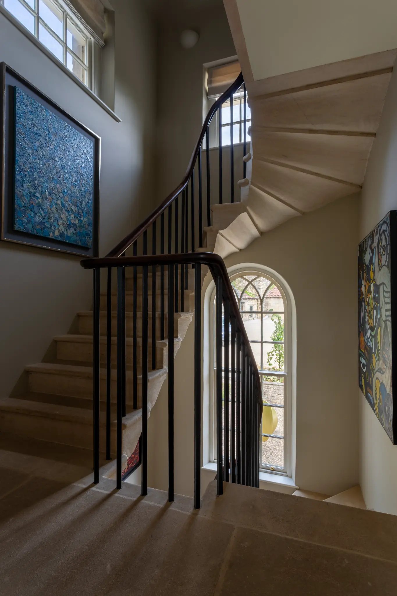 Grand stone staircase with dark wooden handrail and modern abstract paintings on neutral walls inside a luxury Bath manor