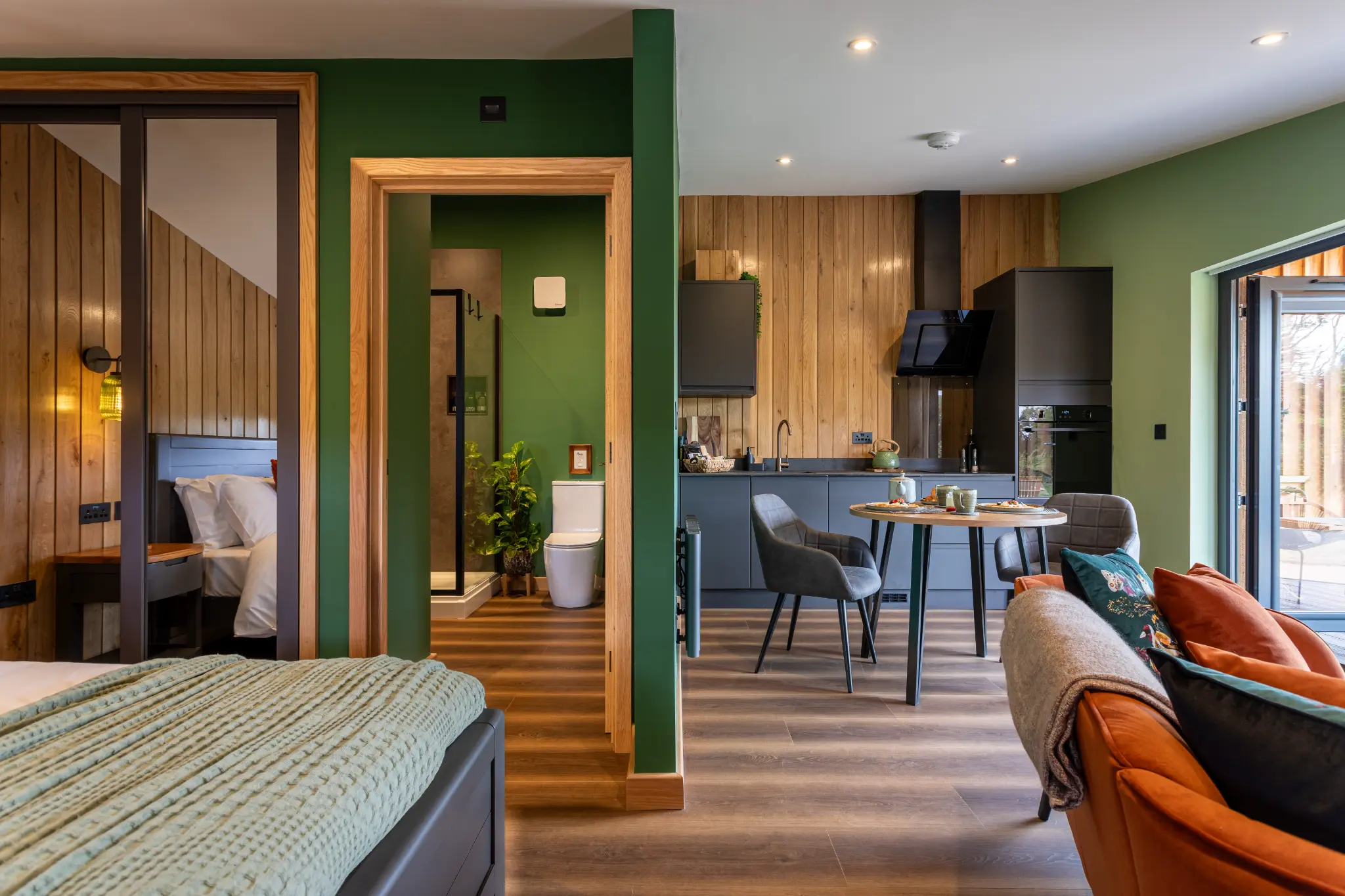 Interior of a luxury lodge looking from the bed past the green feature wall to the kitchen
