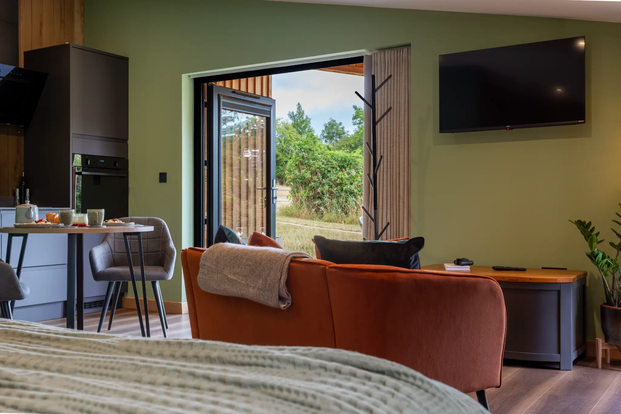 Lounge and dining area of the Ochre Hill cabin with rust sofa and doors open to countryside