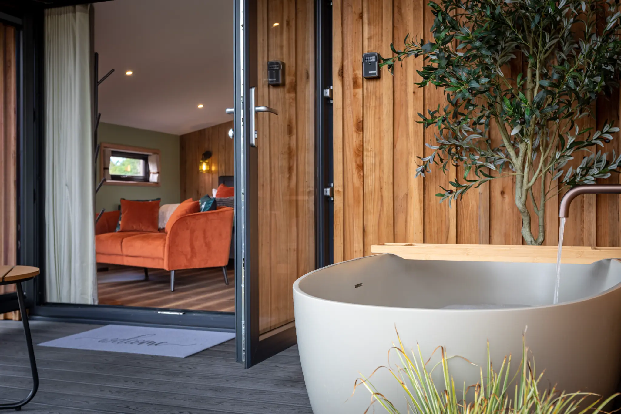 Freestanding outdoor stone bath at Ochre Hill with olive tree and open doors to the lounge