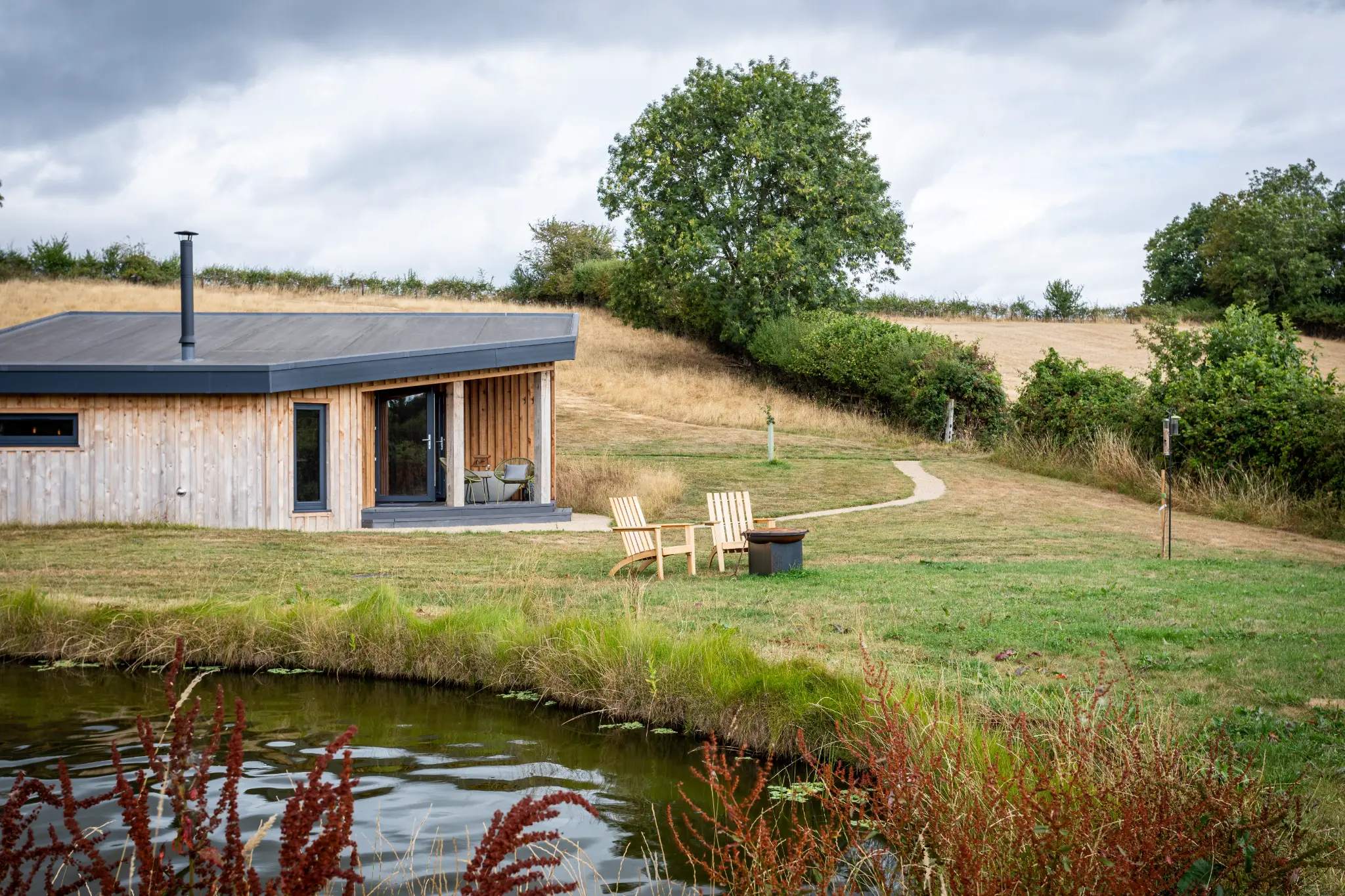 Luxury lodge seen across the pond at Ochre Hill with seating on the bank