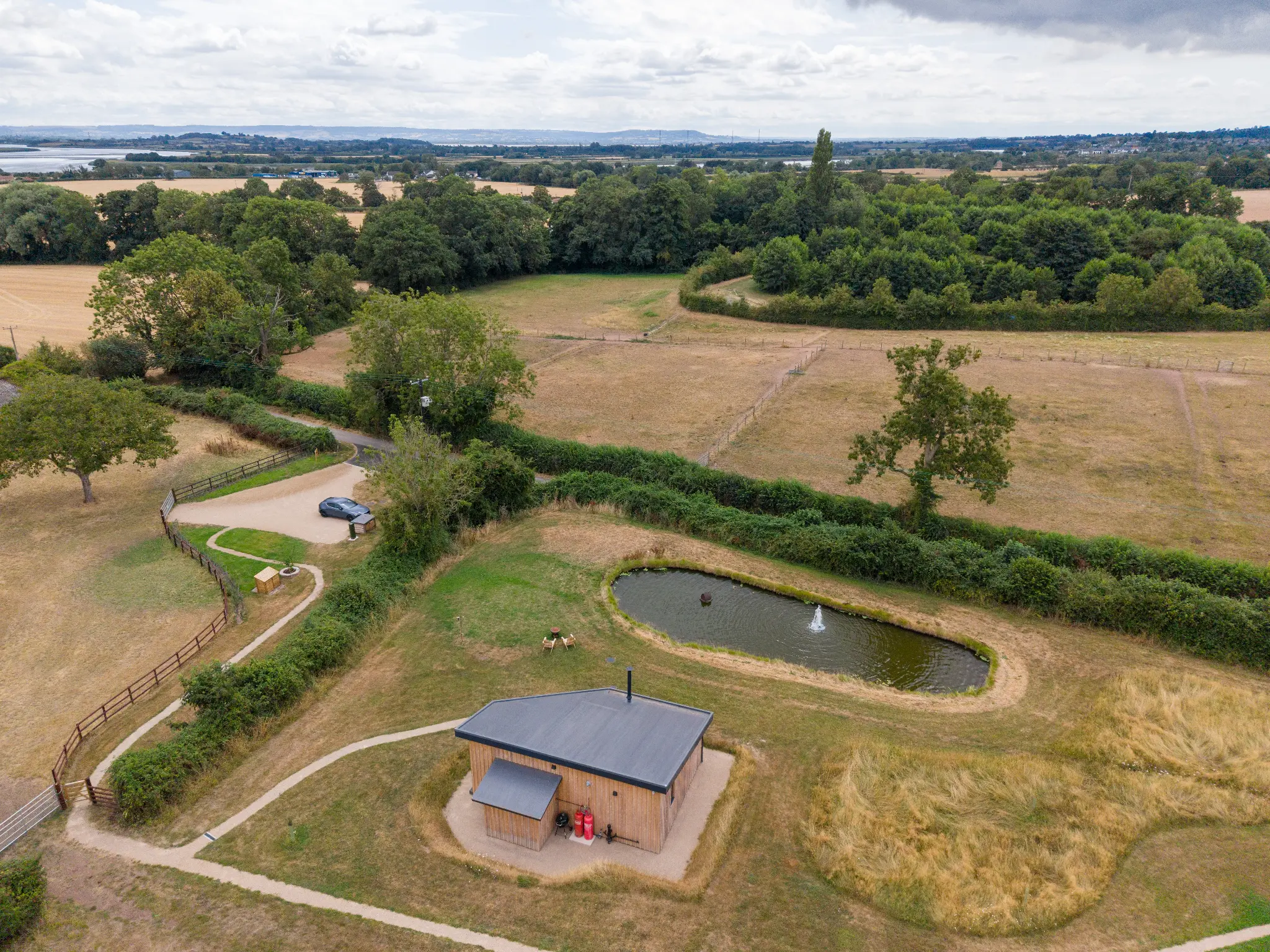 Aerial view of the Ochre Hill lodge and pond set alone in open Gloucestershire countryside