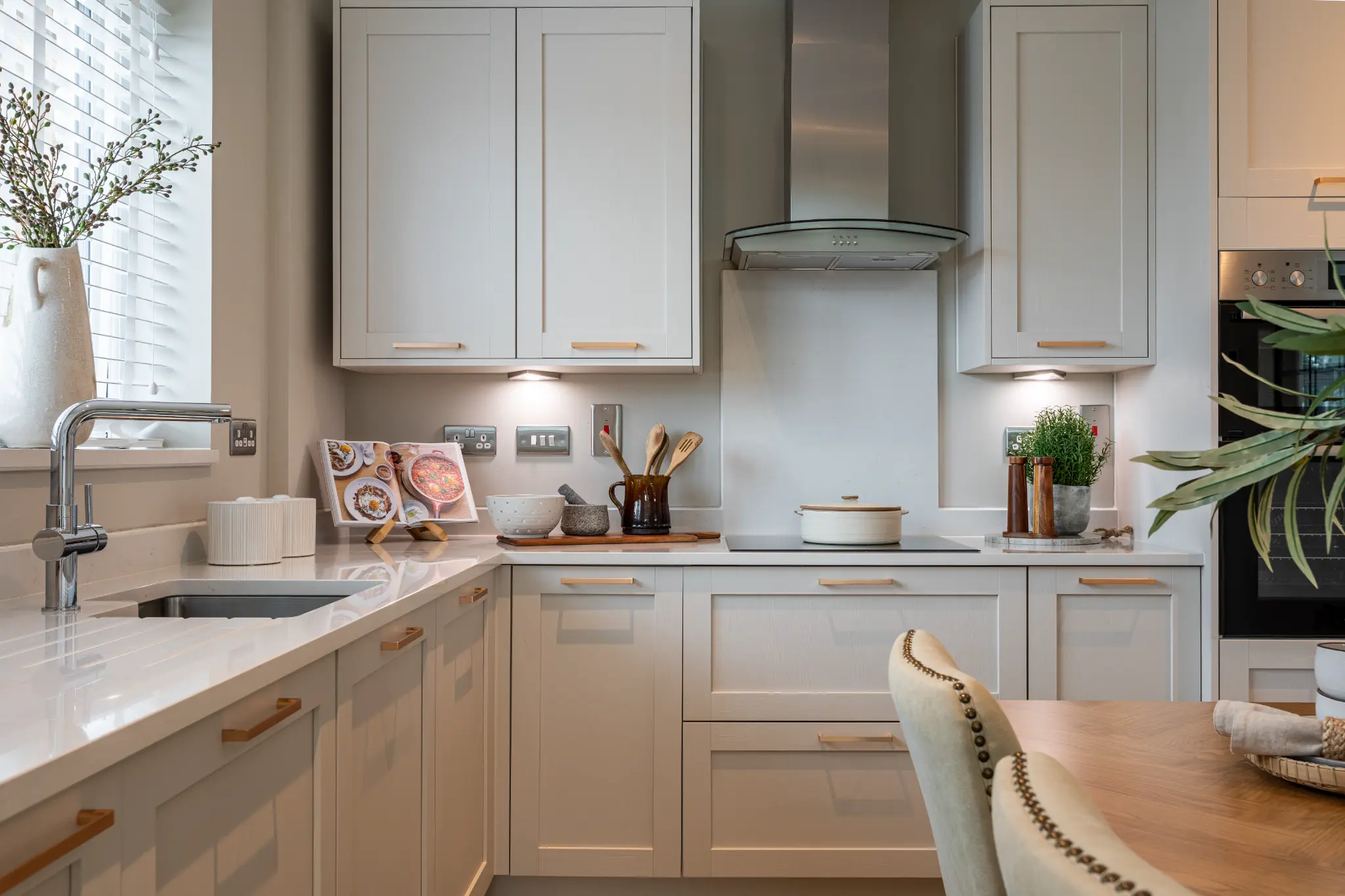 Pale shaker kitchen with brass handles, styled worktops and warm under-cabinet lighting