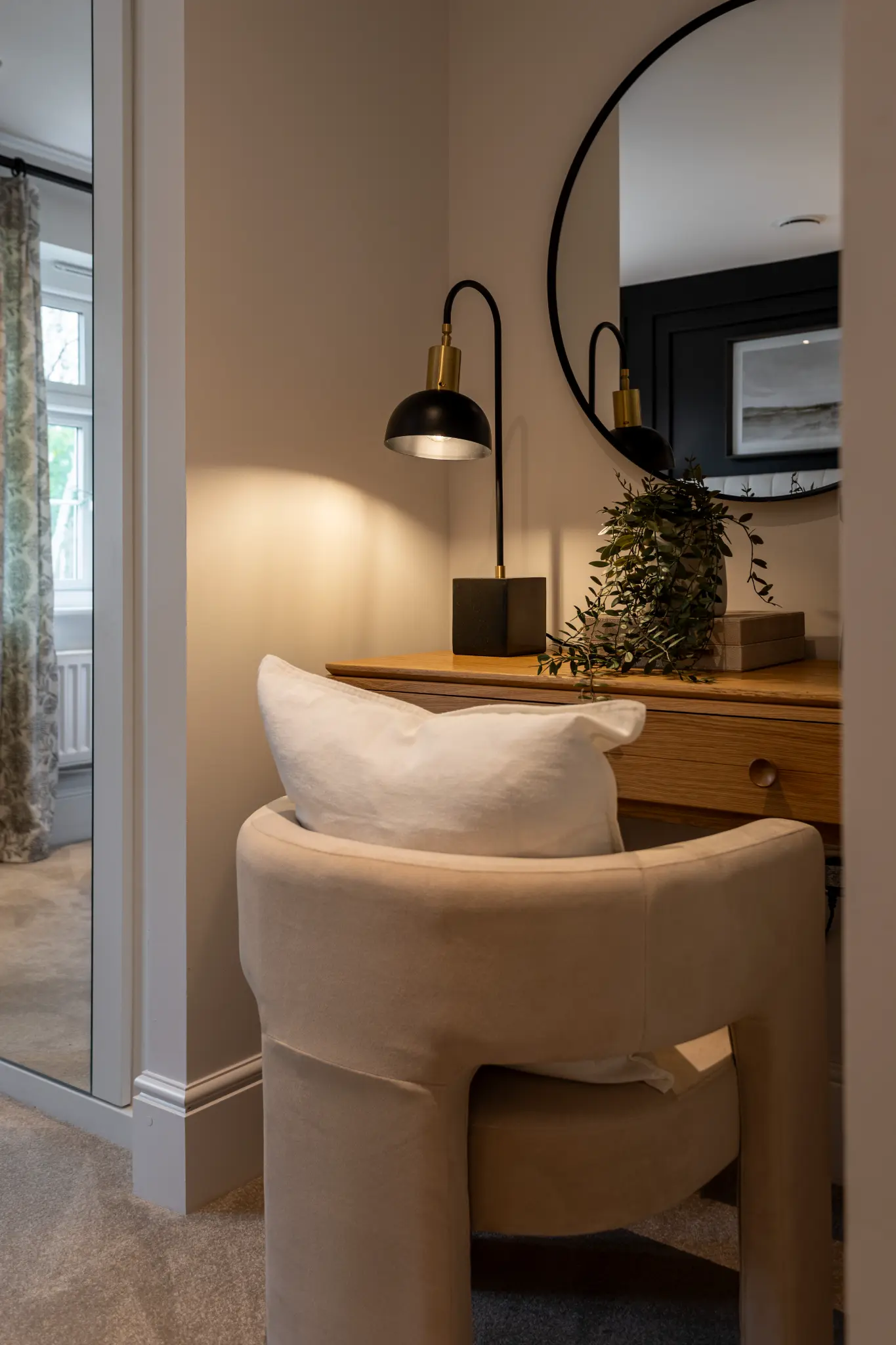 Dressing table detail with warm lamp light, round mirror and foliage in a dressed show home