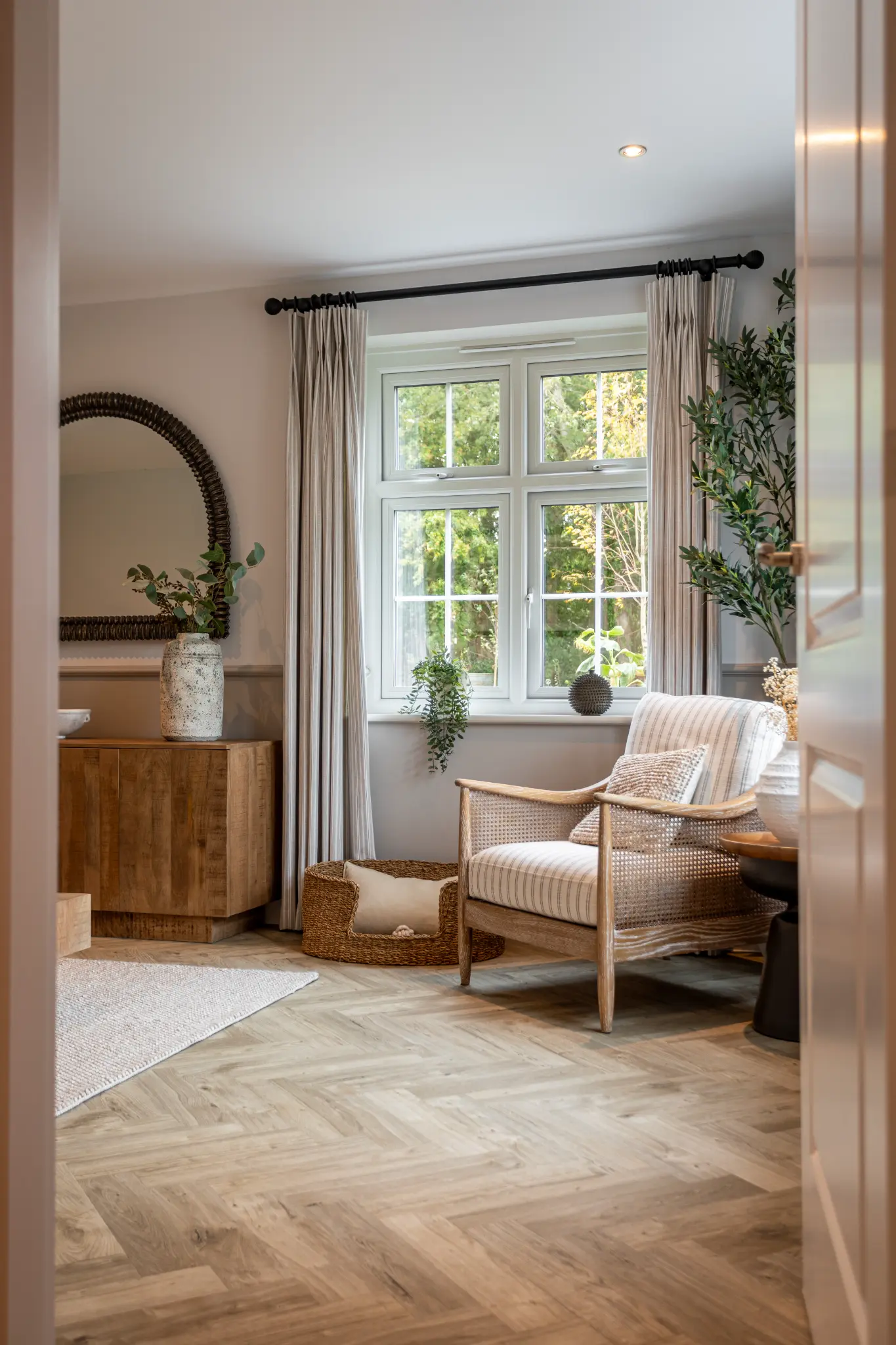 Doorway view into a warm reading room with a cane armchair and natural timber furniture