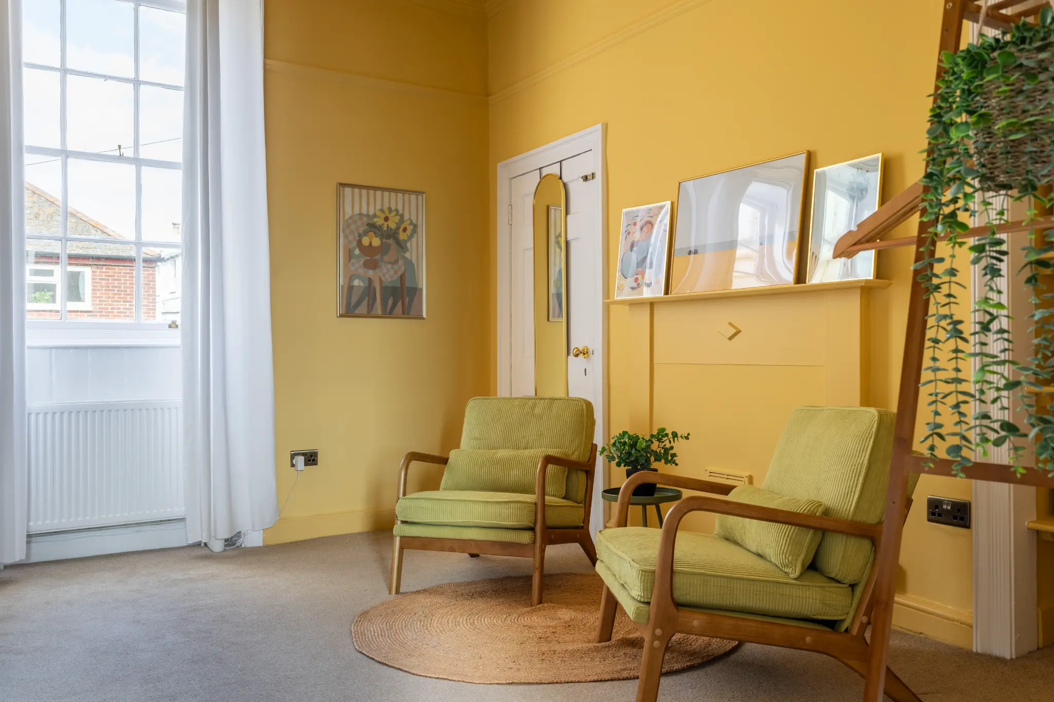Amber bedroom of a Weymouth esplanade Airbnb showing two green cord armchairs, curated art on the walls, and a wooden ladder shelf