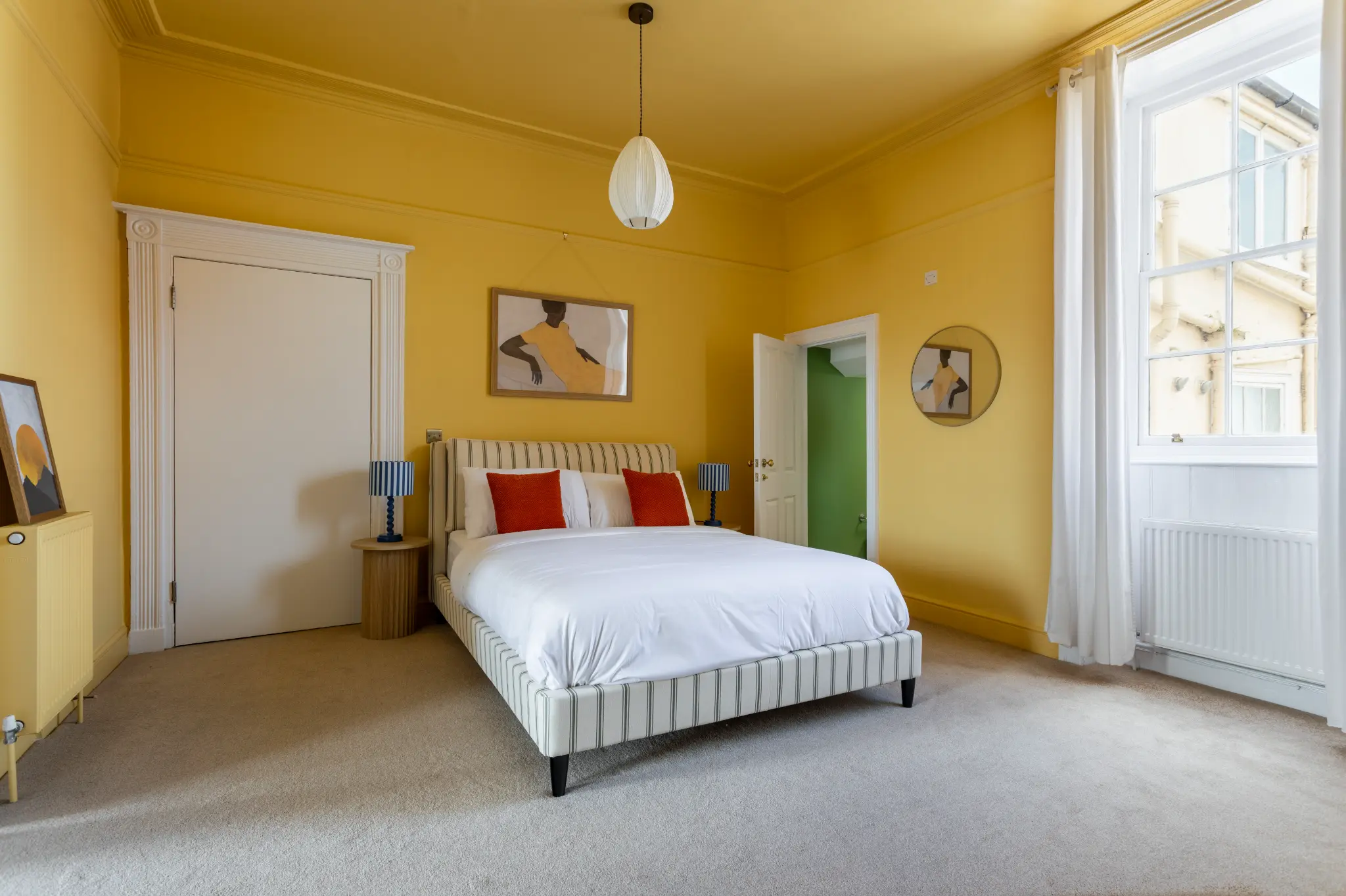 Amber bedroom of a Weymouth esplanade Airbnb with striped bed frame, blue bedside lamps, and figurative artwork above the bed