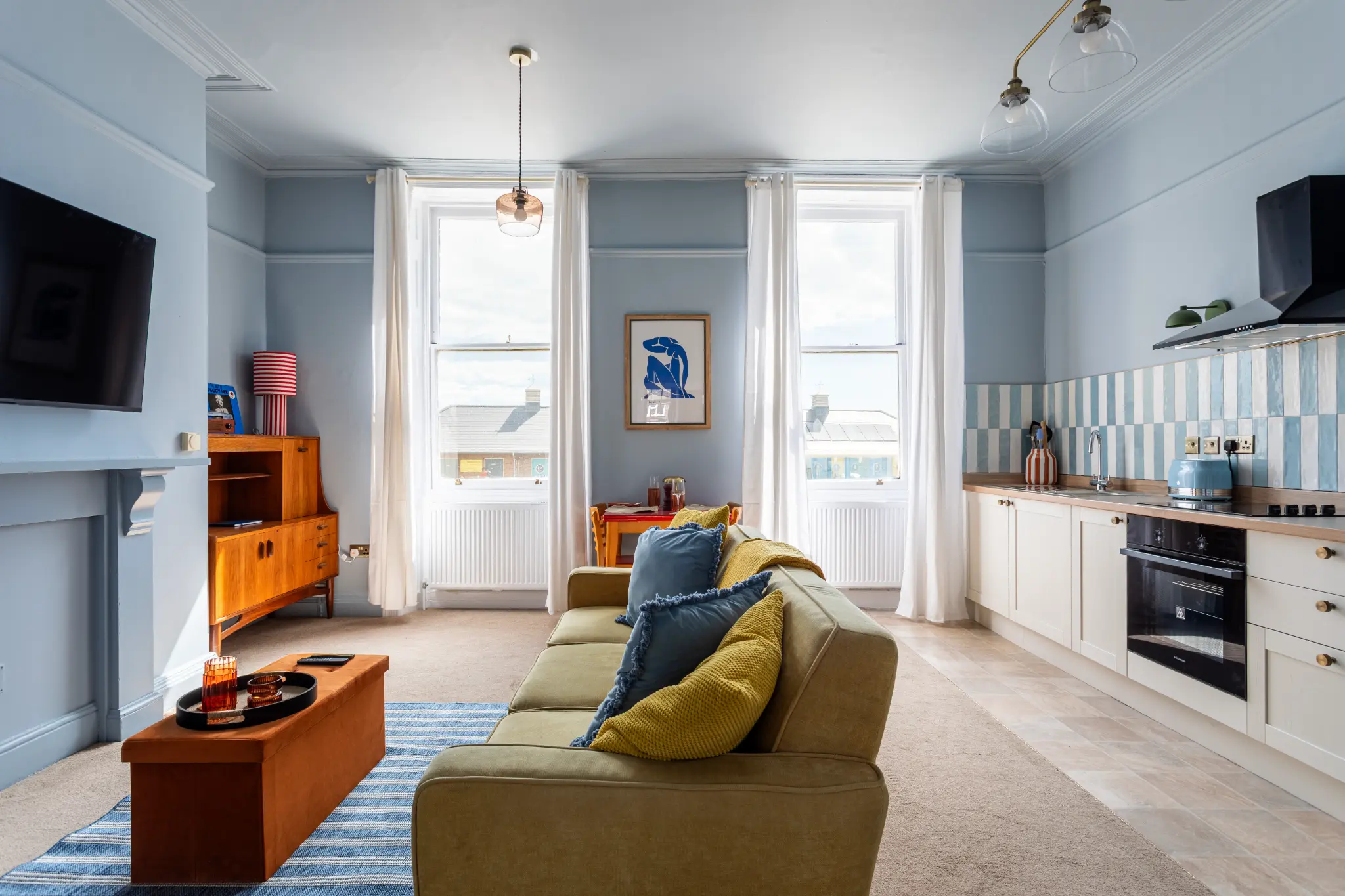 Wide view of the Weymouth esplanade Airbnb showing the open-plan living room and kitchen with two sash windows and coastal light