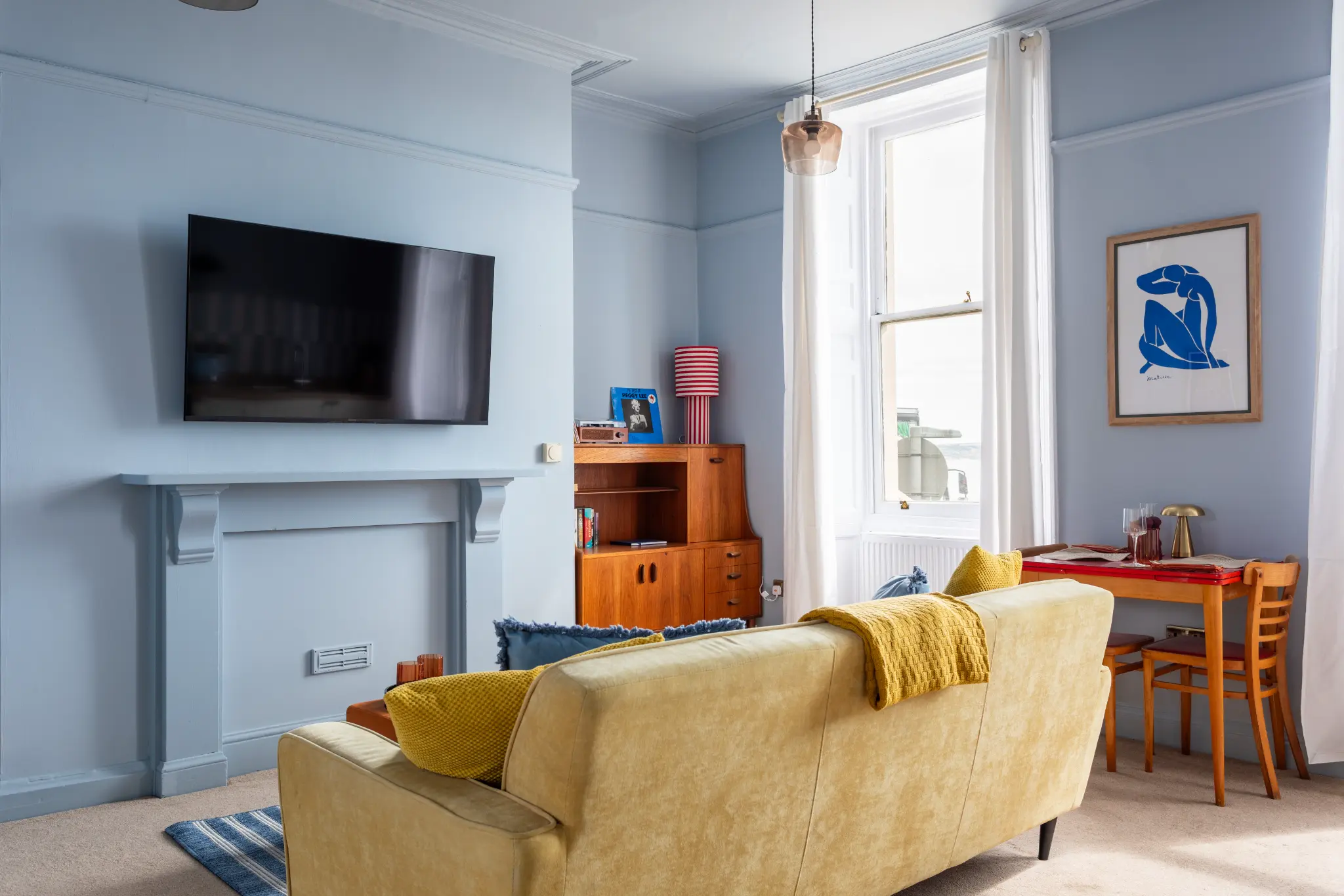 Bohemian Airbnb living room on the Weymouth esplanade with powder blue walls, mustard velvet sofa, and Matisse print