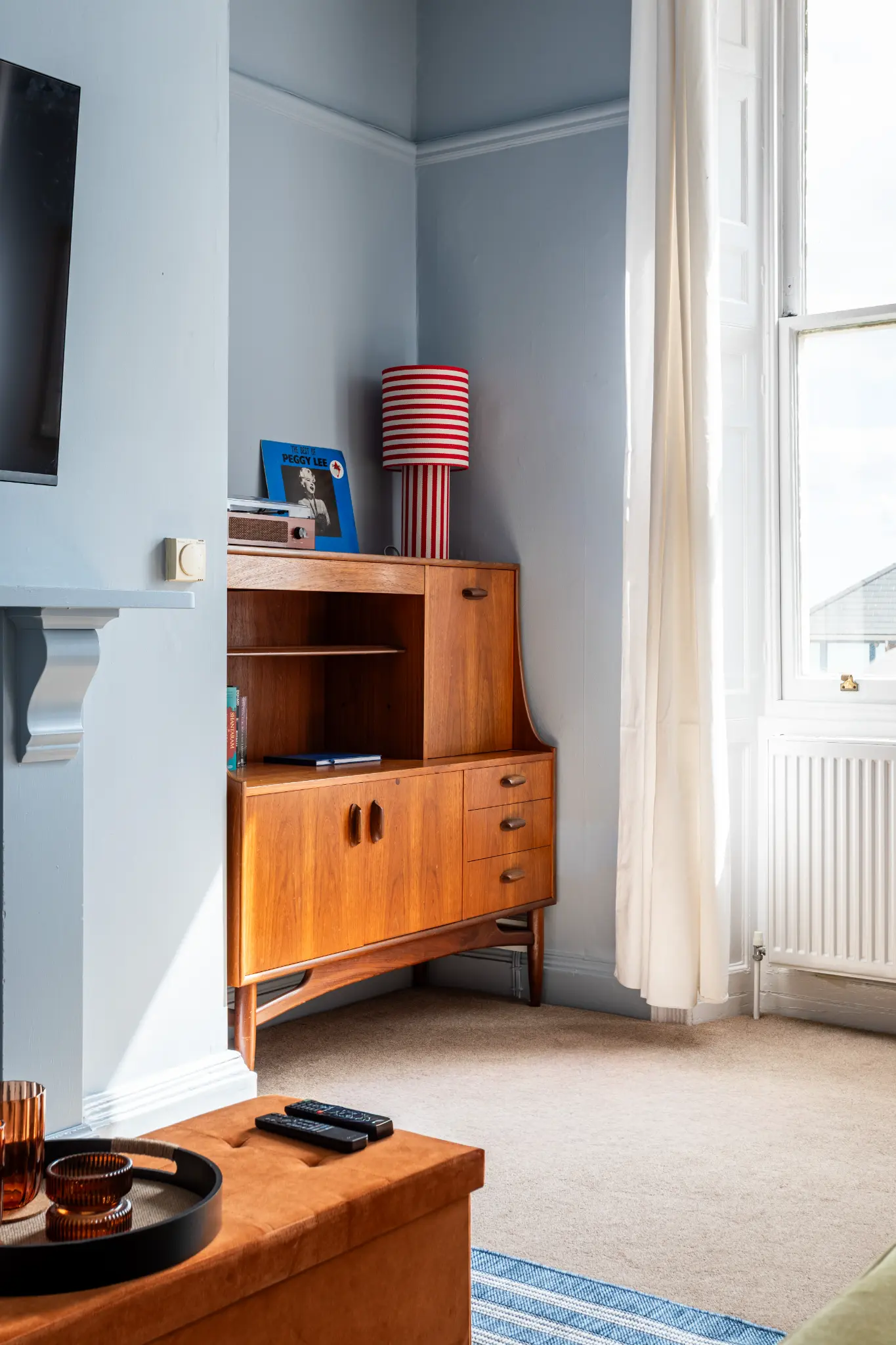 Mid-century teak sideboard with Peggy Lee vinyl, red-striped lamp, and sash window in a Weymouth esplanade Airbnb